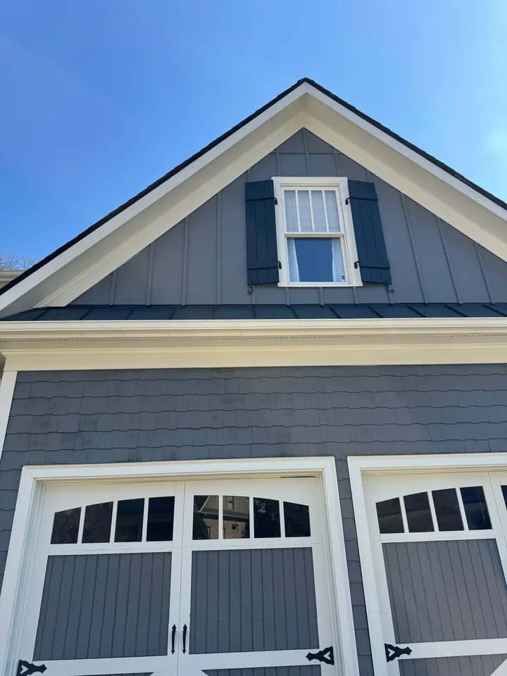 Gray front gable with white trim, a window with dark shutters and garage doors.